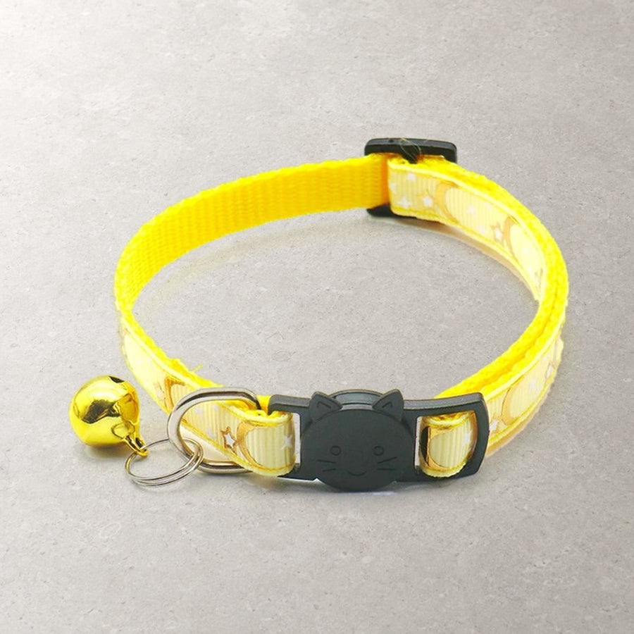 Yellow breakaway cat collar with gold moons and stars, a black cat-face buckle, a D-ring and a gold bell