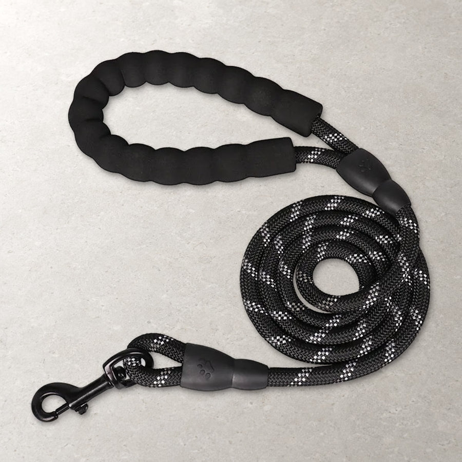 Black reflective rope cat leash coiled on a stone surface, with its padded foam handle and black swivel snap hook